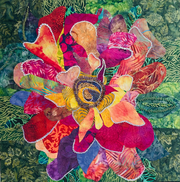 Vibrant flower artwork made with layered fabric and mixed media, featuring an expressive bloom in coral, pink, and yellow  tones with crystal and bead embellishment on a green leafy background 