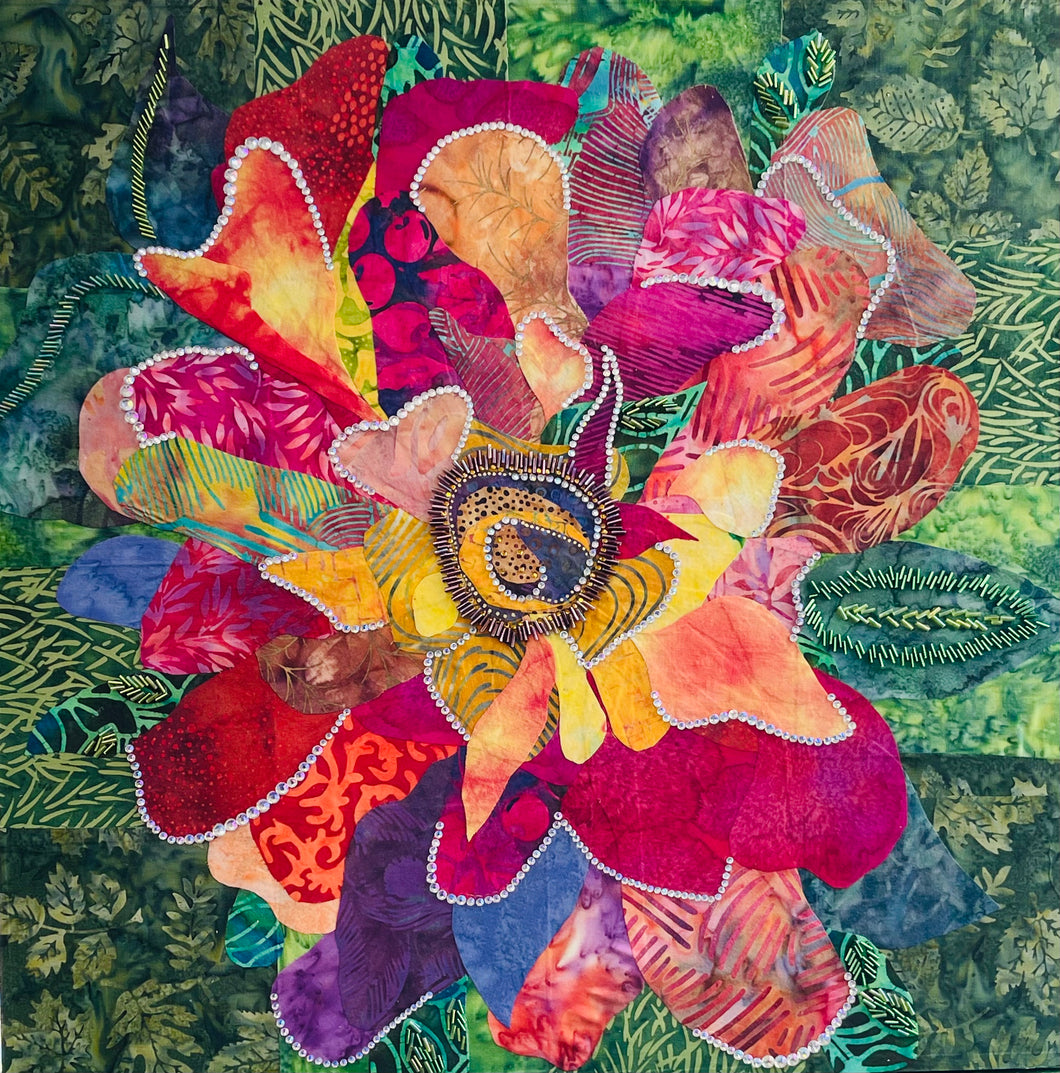 Vibrant flower artwork made with layered fabric and mixed media, featuring an expressive bloom in coral, pink, and yellow  tones with crystal and bead embellishment on a green leafy background 