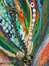 Close detail of found jewelry including brooch and beaded chain woven through gold-foiled petals on Worn Treasure by Robyn Moore Arts, hand-dyed cheesecloth texture beneath acrylic paint