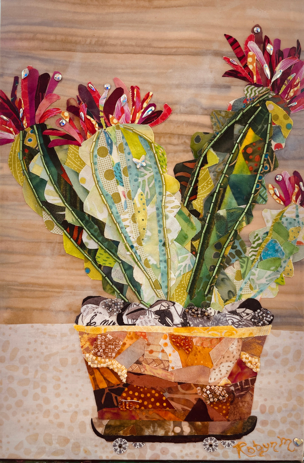 Original potted cactus fabric artwork 8x12 inches, three columnar cacti in patchwork amber rust terracotta fabric pot on fabric wheels with Czech glass bead detail Swarovski crystal blooms in deep magenta crimson pink fabric butterfly detail, wood grain and cream dotted background, birch panel, Floral Botanical Collection, Robyn Moore Arts