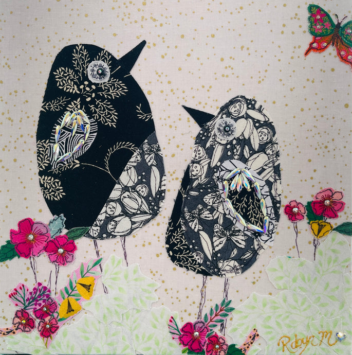 Textile bird art showing two black and white patterned birds surrounded by soft florals in a calm, minimalist composition