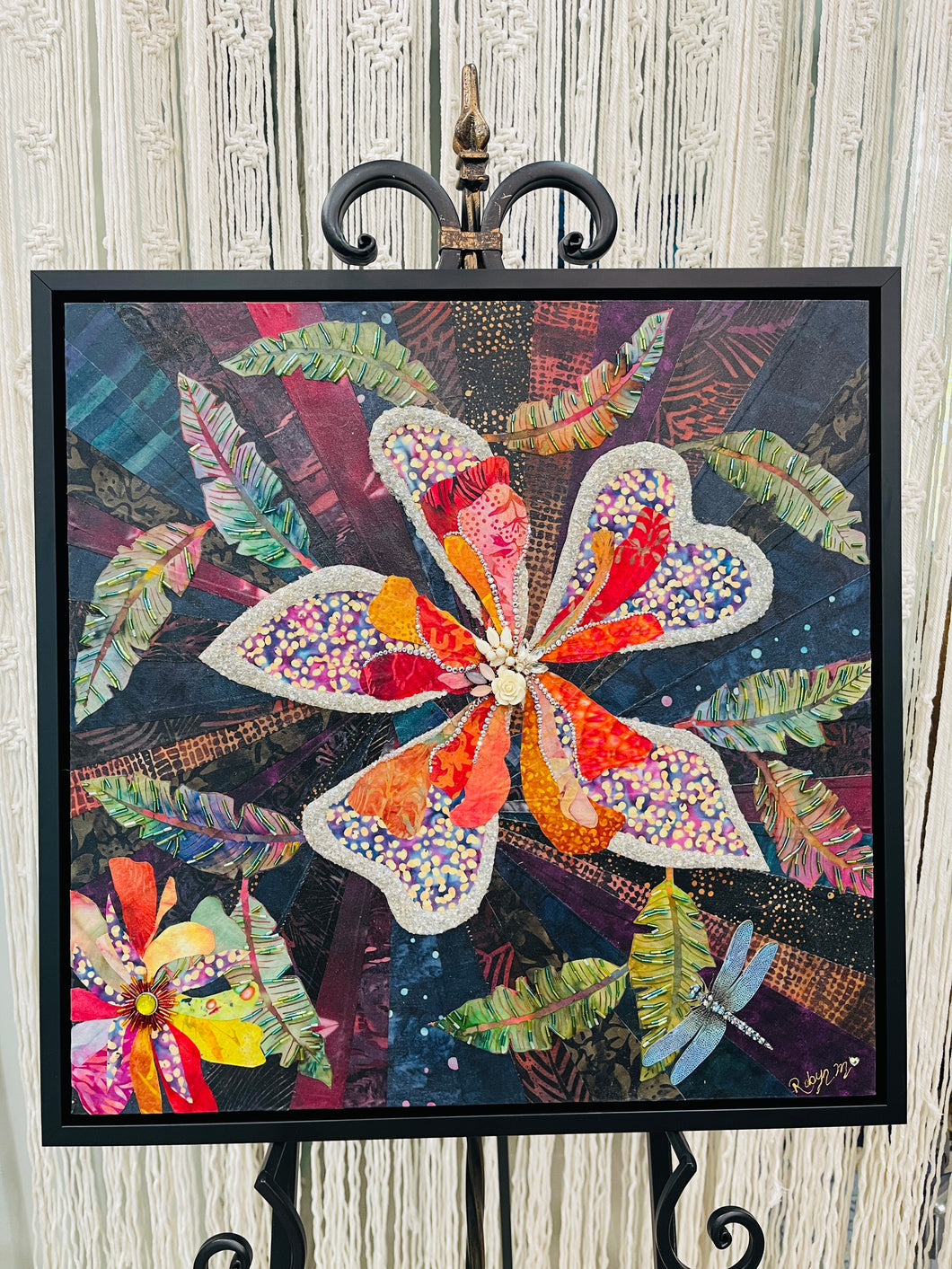 Original mixed media botanical artwork 20x20 inches, large heart-shaped petal flower in violet, coral and crimson batik fabric densely beaded with Czech glass beads and Swarovski crystal outlined edges, vintage rose center embellishment, paper dragonfly detail, deep moody navy and teal fabric background with tropical fronds, on birch panel, part of the Floral and Botanical Collection