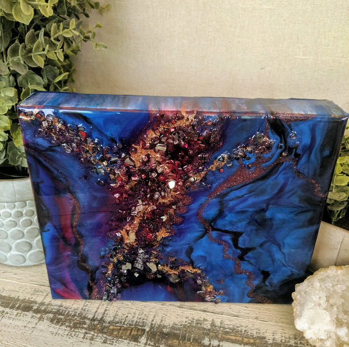 Abstract artwork made with resin and recycled glass on canvas, featuring deep blue and plum tones with red and gold textured central detail
