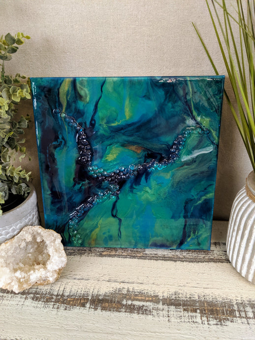 Abstract artwork made with resin and recycled glass on canvas, featuring teal and deep blue tones with a textured, flowing central detail
